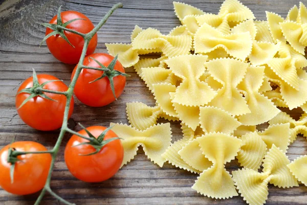 Csomó kis piros cherry paradicsom és a pillangó alakú tészta farfalle fa tábla — Stock Fotó