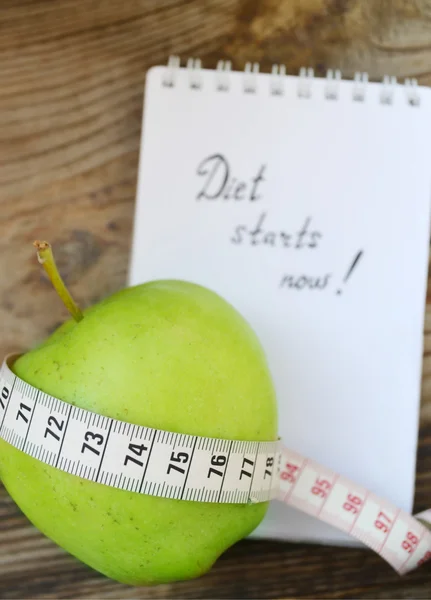 Diet concept with green apple, a notebook and a measuring tape on wooden table — Stock Photo, Image