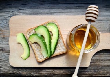 Altın bal honeystick ve ahşap tahta üzerinde yeşil avokado ile sağlıklı bir sandviç ile