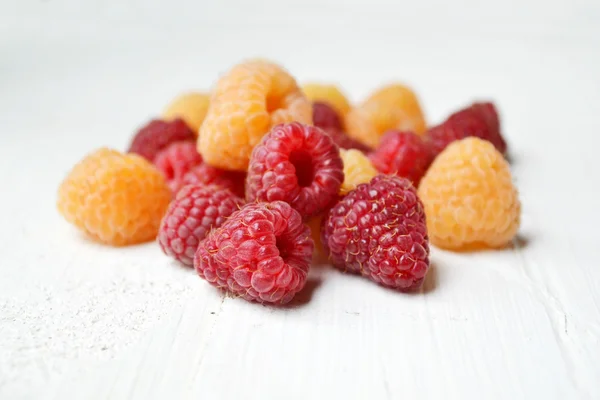 Bright pink and yellow raspberries on white wooden board