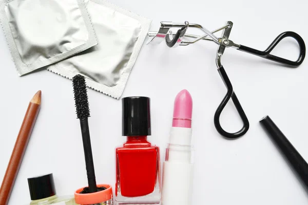 Un par de condones y un conjunto de cosméticos con rímel negro, esmalte de uñas rosa y rojo y lápiz labial y rizador de pestañas aislados en blanco — Foto de Stock