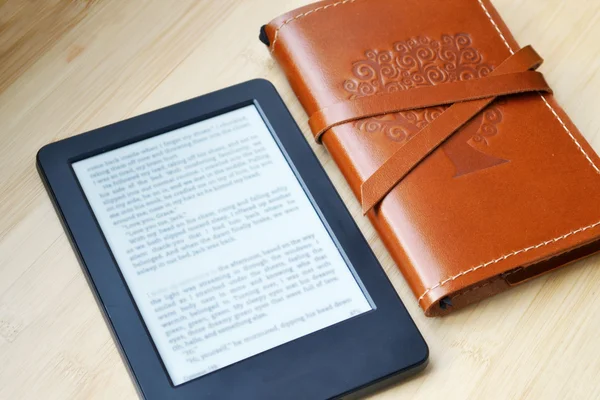 Ahşap masa üzerinde deri kapağı içinde yaşlı bir defter ile siyah ereader