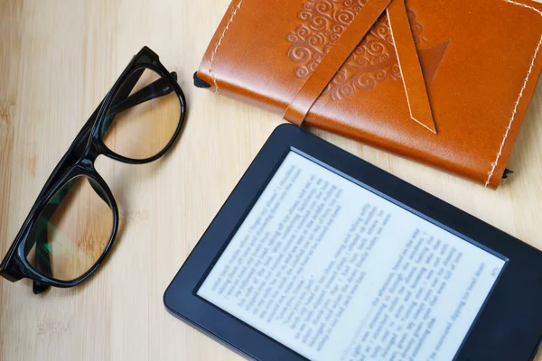 Ereader czarny z czytanie okulary i Starego notebooka w skórzane pokrycie na drewnianym stole — Zdjęcie stockowe