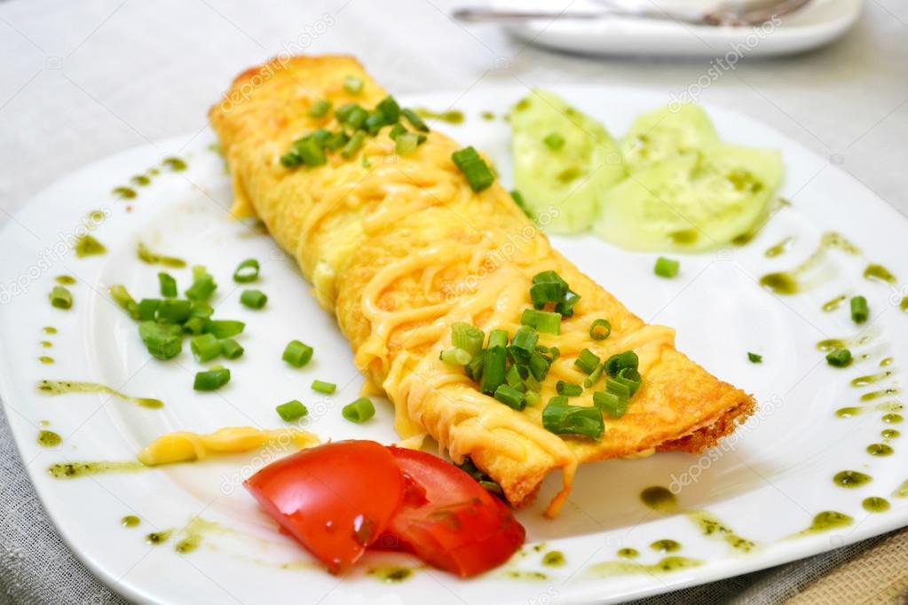 Tasty omelette with cheese and green onion served with tomato on a white plate