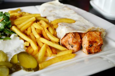 Büyük beyaz tabak tavuk eti pide ekmek, turşu, salata ve sos ile patates kızartması,