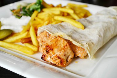 Büyük beyaz tabak tavuk eti pide ekmek, turşu, salata ve sos ile patates kızartması,