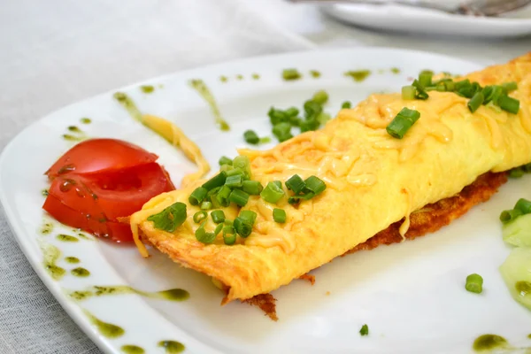 Velsmagende omelet med ost og grønt løg serveret med tomat på en hvid plade - Stock-foto