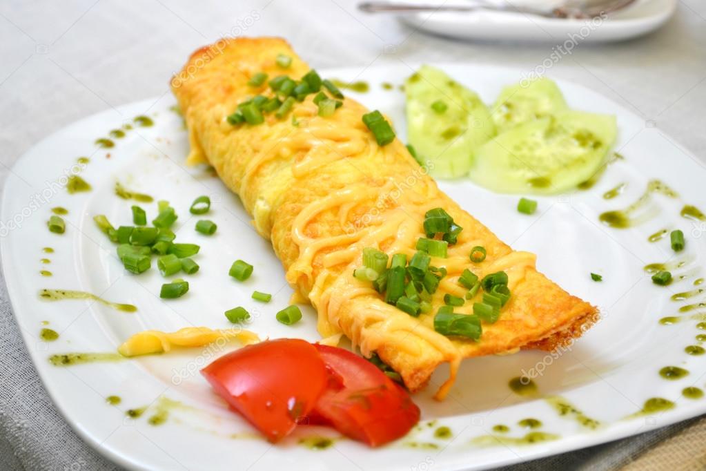 Tasty omelette with cheese and green onion served with tomato on a white plate