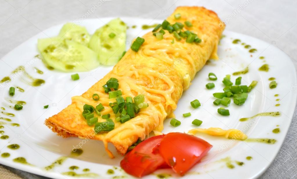 Tasty omelette with cheese and green onion served with tomato on a white plate