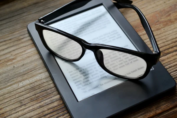 Black ereader with retro glasses on wooden table — Stock Photo, Image