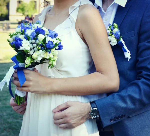 Bräutigam umarmt seine schöne Braut, die einen Hochzeitsstrauß aus Aprikose und blauen Rosen in der Hand hält — Stockfoto