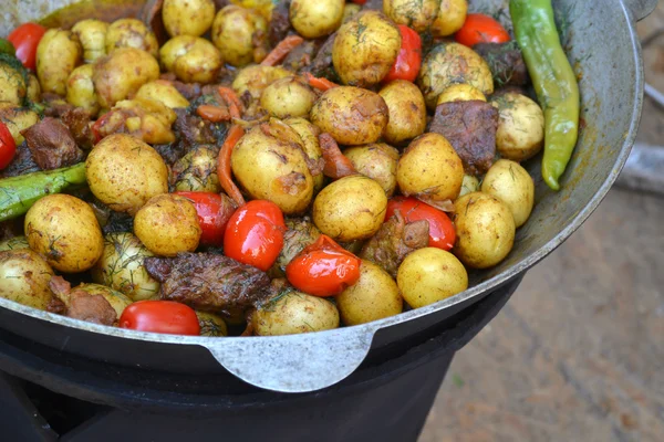 Великий котел зі смаженою картоплею, м'ясом та помідорами — стокове фото