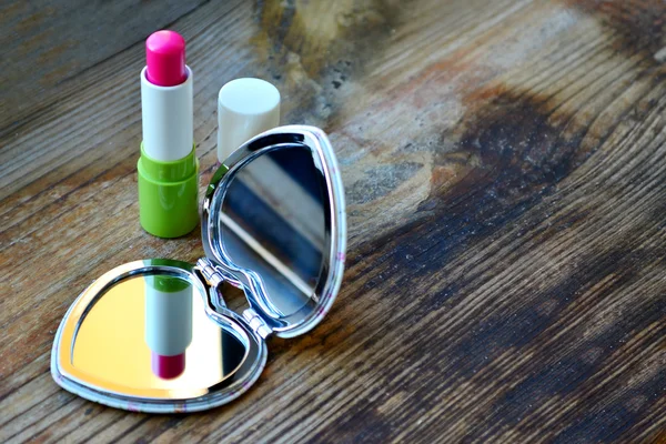 Lindo espejo de bolsillo en forma de corazón con lápiz labial rosa en la mesa de madera — Foto de Stock