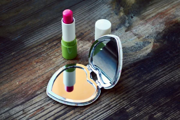 Lindo espejo de bolsillo en forma de corazón con lápiz labial rosa en la mesa de madera — Foto de Stock