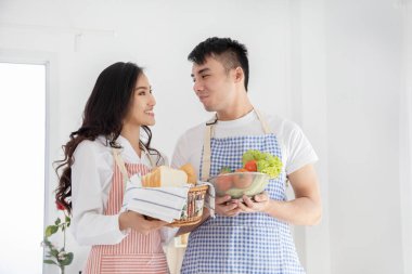 Romantik genç Asyalı çift, beyaz modern mutfakta birlikte yemek pişiriyor.