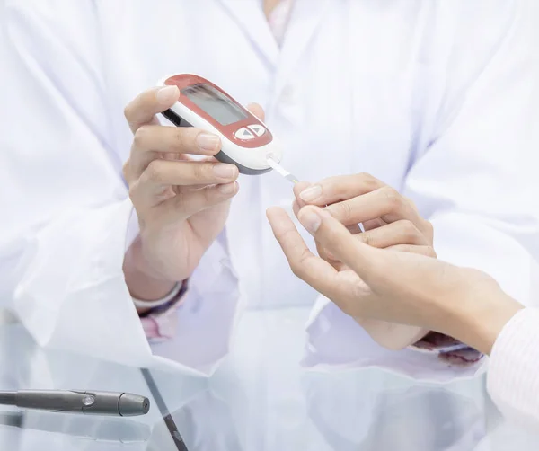 Hands of Pharmacist checking patient blood sugar by glucometer device