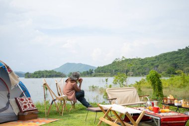 Gölün kıyısında kamp yapan yaşlı adam, emeklilik gününde dinlenmekten mutlu olur.