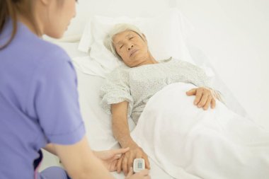 Hemşire yaşlı bir hastanın kanındaki oksijen doygunluğunu ölçmek için nabız oksimetresi kullanıyor.