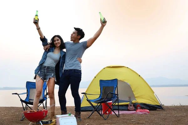 在湖边露营时 一对亚洲夫妇一起在帐篷前喝啤酒 免版税图库图片