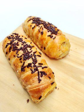 Delicious golden brown Indonesian bolen pisang, a flaky puff pastry filled with sweet banana, topped with chocolate sprinkles, presented on a rustic wooden board.