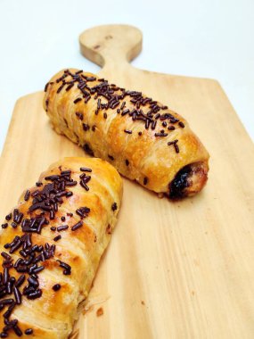 Delicious golden brown Indonesian bolen pisang, a flaky puff pastry filled with sweet banana, topped with chocolate sprinkles, presented on a rustic wooden board.