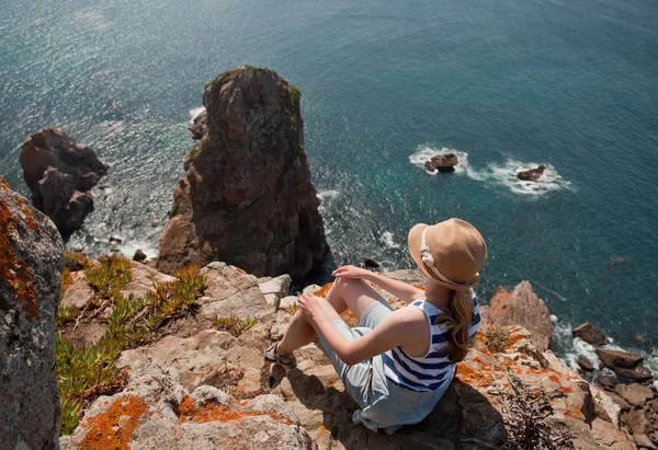 Woman in hat sitting on cabo da roca rocks — Stock Photo, Image