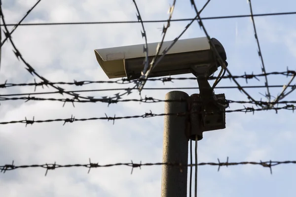 Security camera behind barbed wire fence around prison walls
