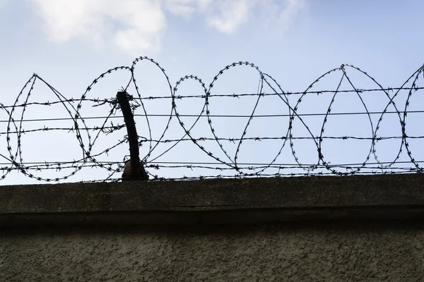 Gevangenis muur prikkeldraad hek met blauwe hemel in achtergrond — Stockfoto