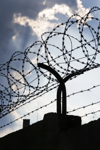 Dramatische wolken achter prikkeldraad hek op gevangenis muur — Stockfoto