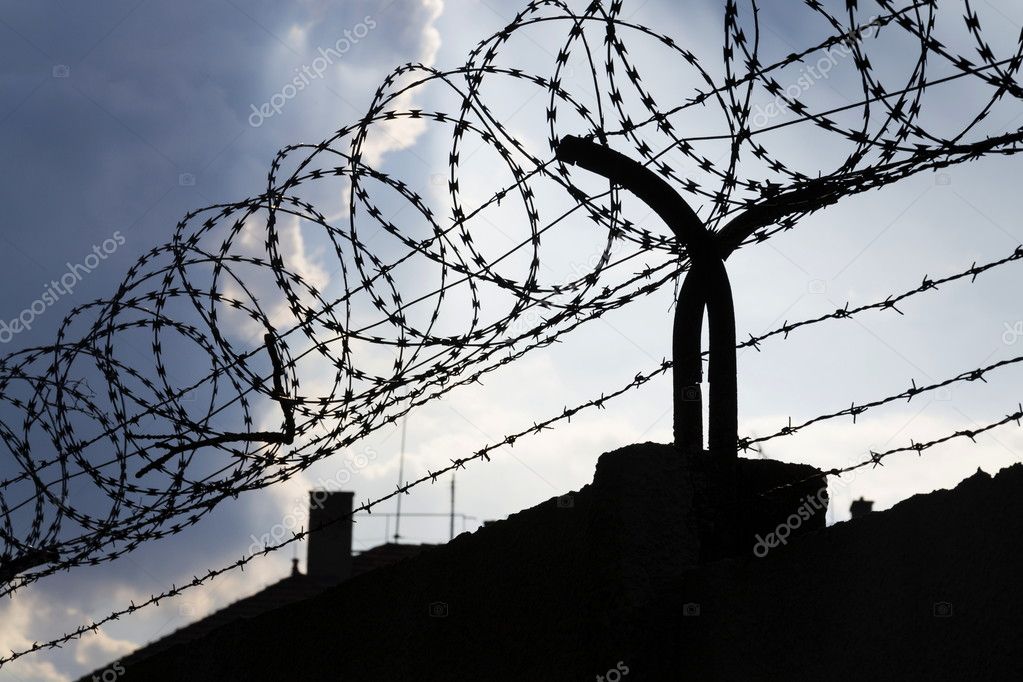 Dramatic clouds behind barbed wire fence on prison wall 