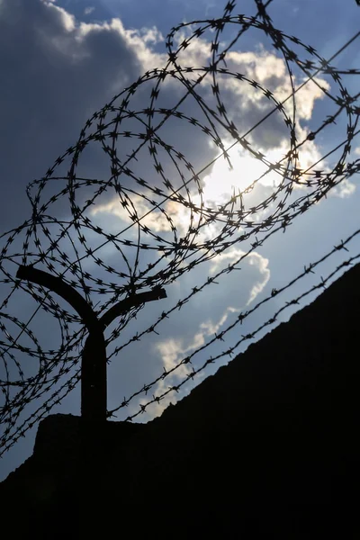 Dramatische wolken achter prikkeldraad hek op gevangenis muur — Stockfoto