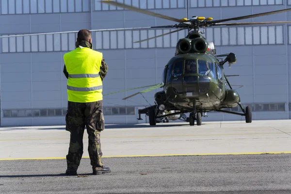 Mies sotilaspuvussa seisoo kiillotetun Mi-8T-helikopterin edessä lentonäytöksen aikana NATO Days — kuvapankkivalokuva