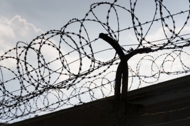 Hapishane duvarlarının etrafındaki dikenli tel örgü. Arka planda mavi gökyüzü.