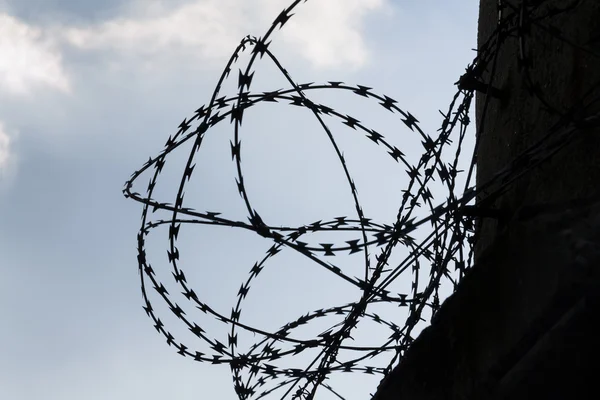 Ogrodzenie z drutu kolczastego wokół więziennych ścian błękitne niebo w tle — Zdjęcie stockowe