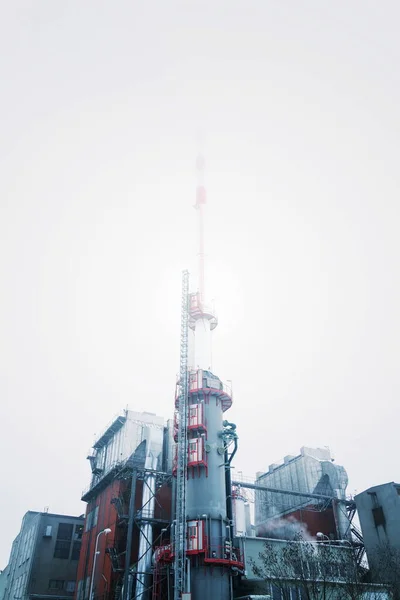 Chimney at heating plant covered in fog, cloudy winter day, low angle view, energy production, air pollution, climate change and global warming concept