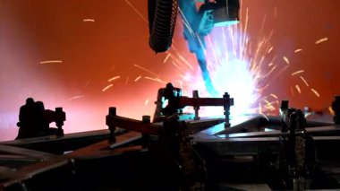 Turuncu arka planda hareket eden robotik kaynak kolu, modern endüstriyel otomasyonu, hassas mühendisliği ve Endüstri 4.0 teknolojisini sembolize eden gerçek zamanlı video.