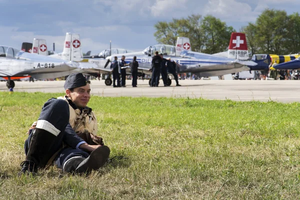 Hombre en uniforme de piloto vintage sonriendo con el equipo suizo Pilatus aerobatic P3 Flyers en segundo plano —  Fotos de Stock