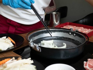 Aşçı restoarant mutfak maskesi mavi eldiven takıyor. Yemek çubuğu shabu suki açık büfesi sağlıklı sebze domuz eti müşterisi Asya Japon Çin porselenleri covid-19 hastalığını korumak için sıcak yemek yiyor.