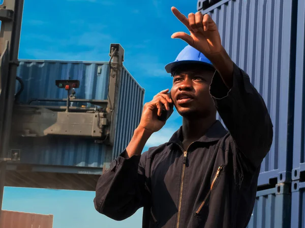 Foreman engineer manager  african blue hat black shadow safety talk telephone look pointing finger work report warehouse terminal container import export business customer logistic  international