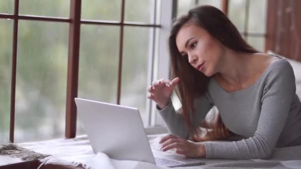 一个年轻的女人躺在床上 看着手提电脑的屏幕 直着头发 远程工作 舒适的工作场所 — 图库视频影像