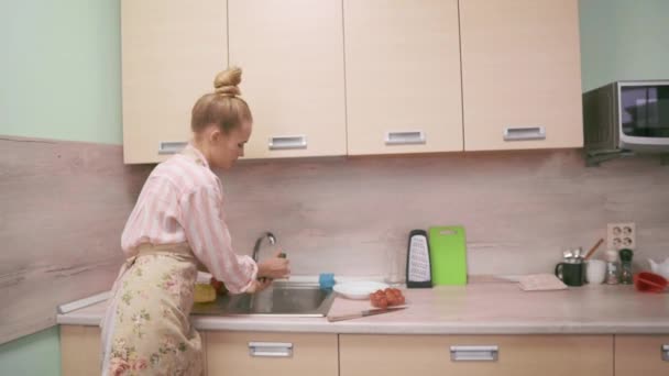 Eine junge Frau in Schürze wäscht Gemüse in der Spüle — Stockvideo