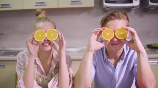 Hombre y mujer sostienen naranjas cortadas delante de sus ojos — Vídeos de Stock