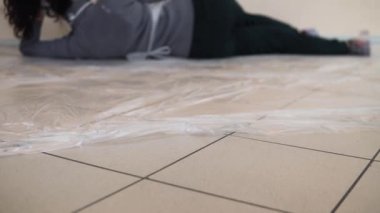 Uzanan bir kız boyasız bir duvara turuncu boya sürüyor.