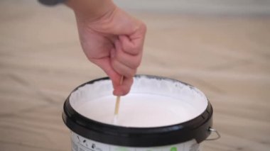 İşçi sopayla kovada beyaz boya karıştırıyor.