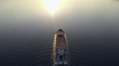 Yük nehri taşımacılığı nehirde güneşe doğru yüzer. Gemiden gelen suyun üzerinde iz var. Yukarıdan bak. Helikopterden ateş ediliyor.