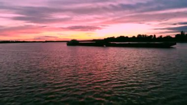 Yük nehri taşımacılığı, parlak bir günbatımı gökyüzünün arka planına karşı nehirde yüzer. Harika bir yaz manzarası. Helikopterden ateş ediliyor.