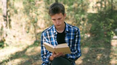 Mavi gömlekli adam güneşli bir günde parkta otururken kitap okur. Keyifli zaman geçirme. Parkta dinlen. Açık havada kitap okuyorum.