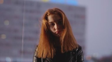 Gözlerinin altında maskara olan genç bir kadın pencerenin önünde oturur ve üzgün bir şekilde kameraya bakar.