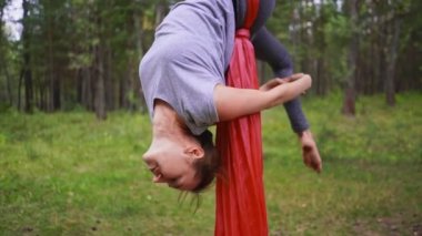 Yoga hamağında baş aşağı asılı duran ve sırtını kamburlaştıran bir kadın. Açık hava sporları