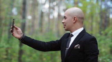 Takım elbiseli bir adam parkta dikilirken telefonla konuşuyor.